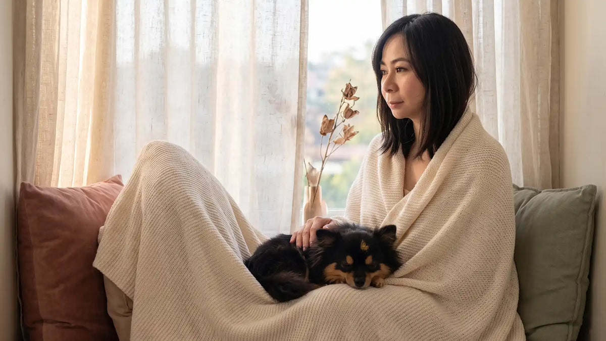 A sensitive woman resting safely by a window with a small dog asleep nearby